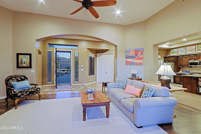 living room featuring hardwood / wood-style flooring, ceiling fan, and a towering ceiling