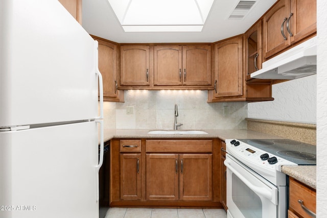 kitchen featuring white appliances, visible vents, brown cabinetry, under cabinet range hood, and a sink