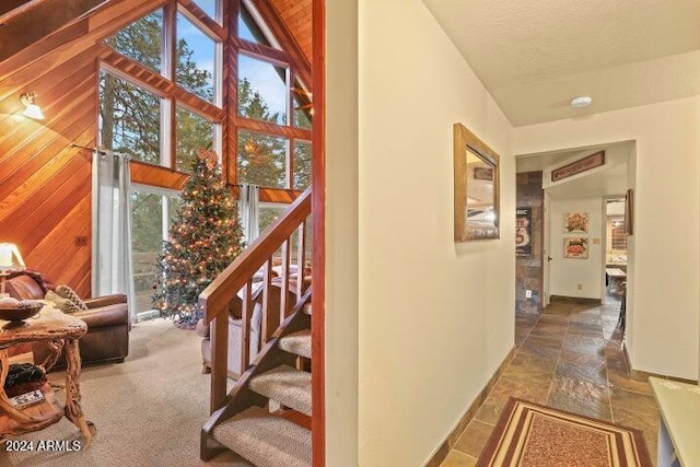 stairs with carpet flooring, wood walls, and high vaulted ceiling