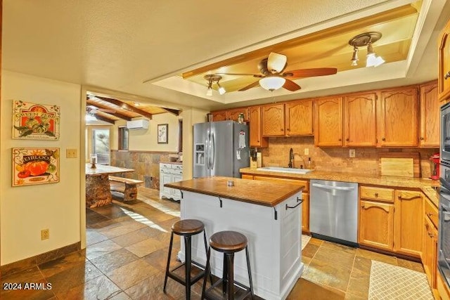 kitchen with ceiling fan, sink, a wall mounted AC, a kitchen bar, and appliances with stainless steel finishes