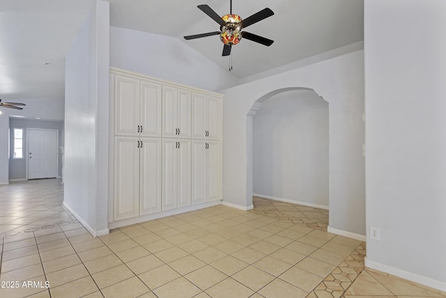 unfurnished room featuring ceiling fan, arched walkways, vaulted ceiling, light tile patterned floors, and baseboards
