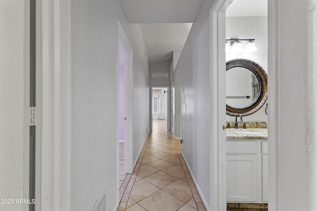 hall with baseboards, a sink, and light tile patterned flooring