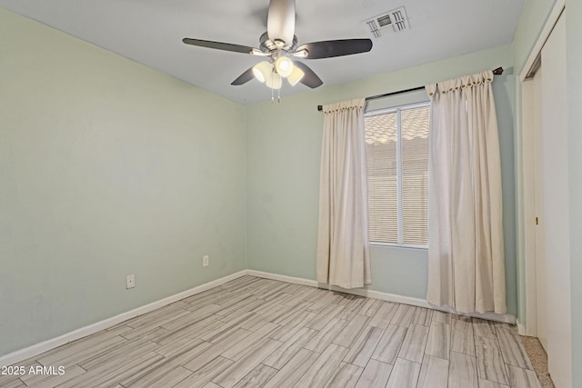 empty room featuring a ceiling fan, baseboards, visible vents, and light wood-type flooring