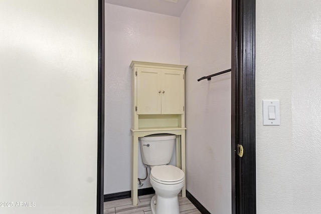 bathroom with toilet, baseboards, and wood finished floors