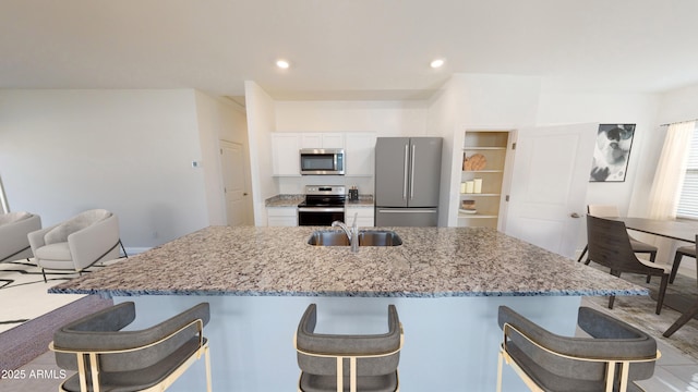 kitchen featuring sink, white cabinetry, a kitchen island with sink, stainless steel appliances, and light stone counters