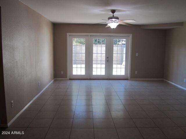 empty room with french doors, dark tile patterned floors, and ceiling fan