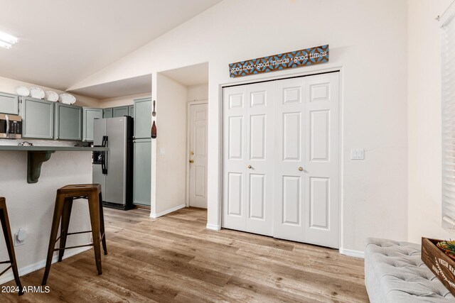 kitchen with light wood-type flooring, appliances with stainless steel finishes, lofted ceiling, and a breakfast bar area