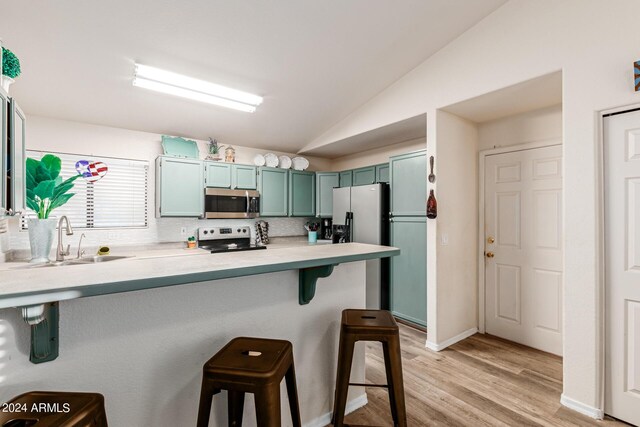 kitchen featuring light wood-type flooring, appliances with stainless steel finishes, sink, lofted ceiling, and a kitchen bar