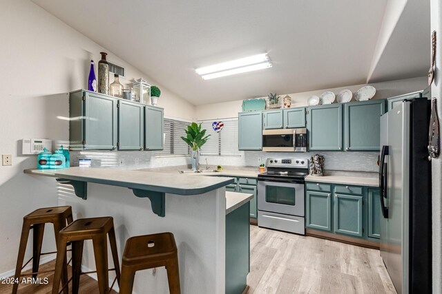 kitchen featuring appliances with stainless steel finishes, kitchen peninsula, a breakfast bar area, and light hardwood / wood-style floors