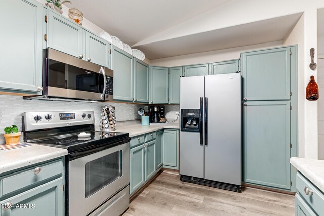 kitchen featuring blue cabinetry, backsplash, stainless steel appliances, lofted ceiling, and light hardwood / wood-style floors