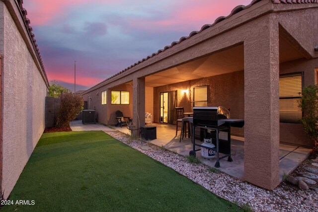 back house at dusk with a yard, a patio area, and central air condition unit