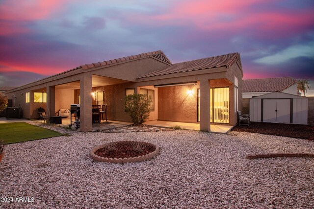 back house at dusk featuring an outdoor fire pit, central AC unit, a storage unit, and a patio area