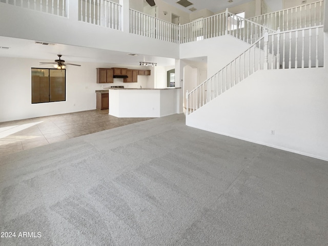 unfurnished living room with ceiling fan, carpet floors, and a high ceiling