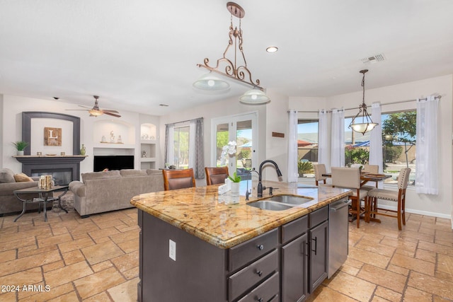 kitchen featuring light stone countertops, sink, decorative light fixtures, a center island with sink, and dishwasher