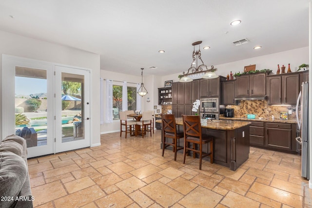 kitchen with hanging light fixtures, a kitchen breakfast bar, an island with sink, decorative backsplash, and dark brown cabinets