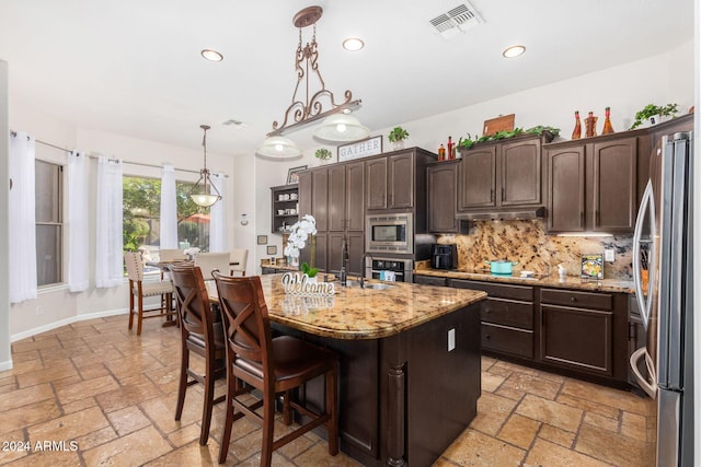 kitchen with pendant lighting, a center island with sink, decorative backsplash, appliances with stainless steel finishes, and dark brown cabinetry