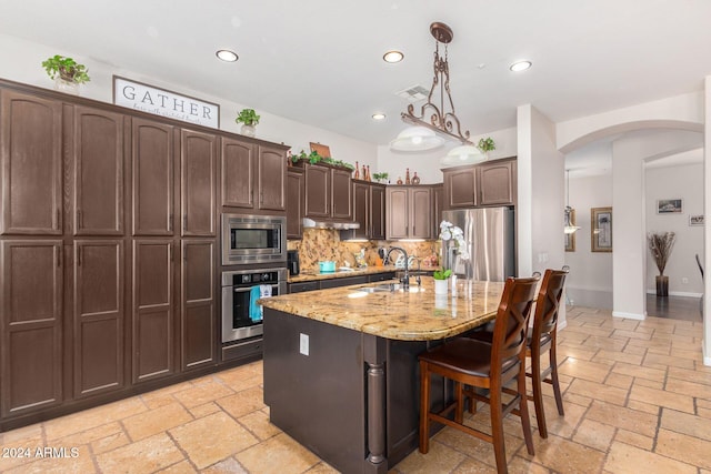 kitchen with light stone countertops, tasteful backsplash, stainless steel appliances, sink, and an island with sink