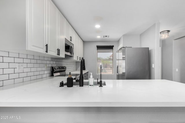 1180 W Rosal Ave, Apache Junction, AZ 85120 - kitchen with appliances with stainless steel finishes, a peninsula, decorative backsplash, white cabinetry, and light stone counters