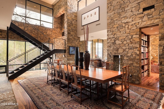 dining area with a healthy amount of sunlight, a towering ceiling, and hardwood / wood-style flooring