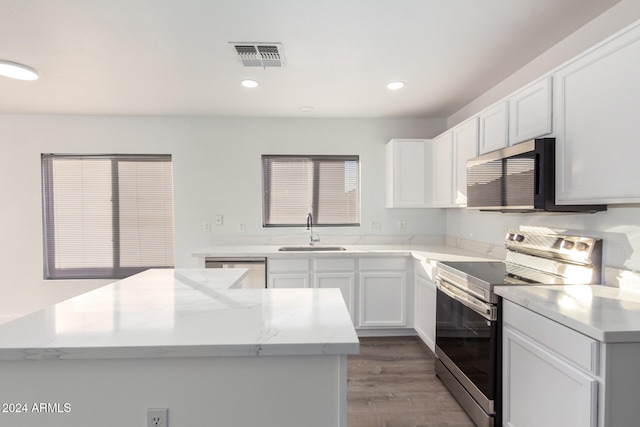 kitchen featuring appliances with stainless steel finishes, light wood-type flooring, light stone counters, sink, and white cabinetry