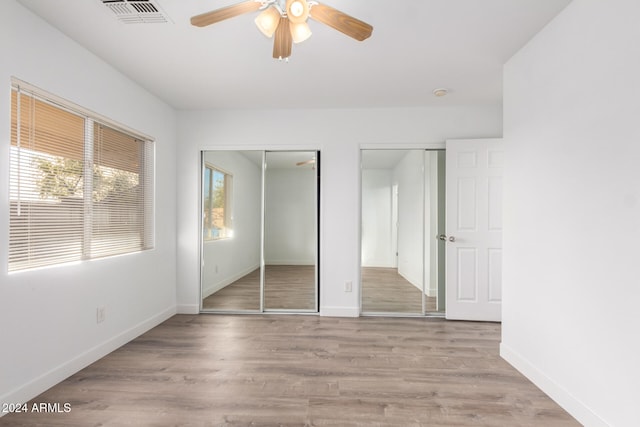 unfurnished bedroom featuring light wood-type flooring, ceiling fan, and multiple closets