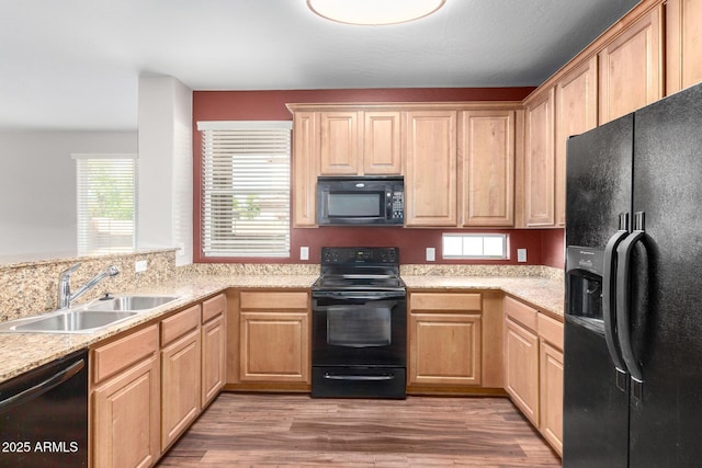 kitchen with black appliances, a sink, light brown cabinetry, light wood-style flooring, and light stone counters