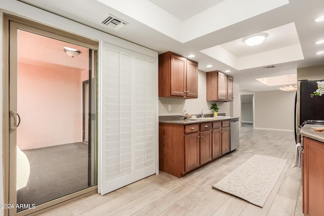 kitchen with light wood-type flooring, dishwasher, a tray ceiling, and sink