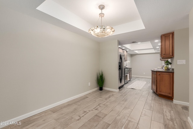 interior space featuring light hardwood / wood-style floors, stainless steel fridge with ice dispenser, hanging light fixtures, an inviting chandelier, and a raised ceiling