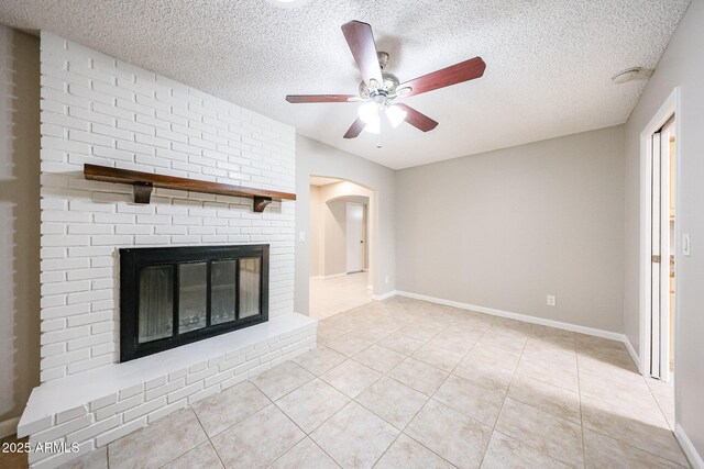 7439 E Ed Rice Ave, Mesa, AZ 85208 - unfurnished living room with ceiling fan, a textured ceiling, light tile patterned floors, a brick fireplace, and arched walkways