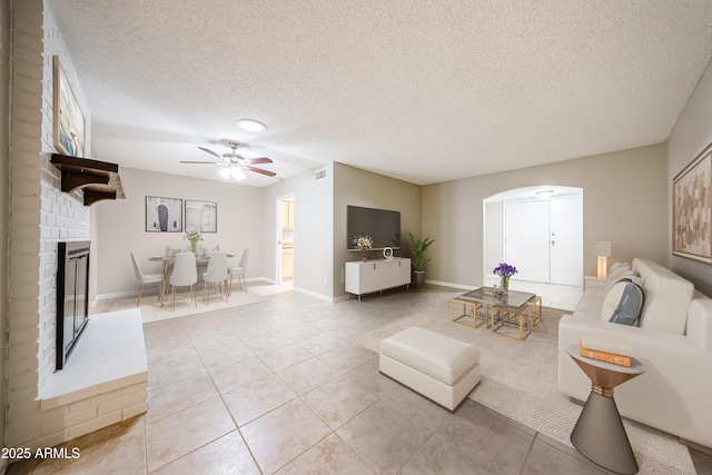 7439 E Ed Rice Ave, Mesa, AZ 85208 - living room with ceiling fan, arched walkways, light tile patterned floors, a fireplace, and a textured ceiling