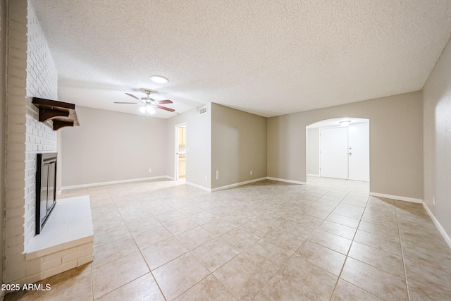 7439 E Ed Rice Ave, Mesa, AZ 85208 - unfurnished living room with arched walkways, light tile patterned floors, ceiling fan, a brick fireplace, and a textured ceiling