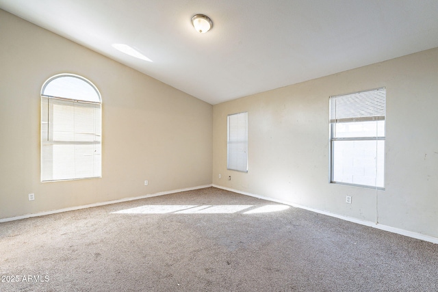 carpeted empty room featuring baseboards and vaulted ceiling