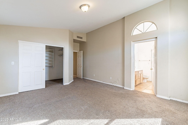 unfurnished bedroom with lofted ceiling, light carpet, visible vents, baseboards, and a closet