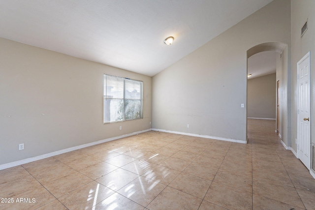 unfurnished room with vaulted ceiling, light tile patterned flooring, arched walkways, and baseboards