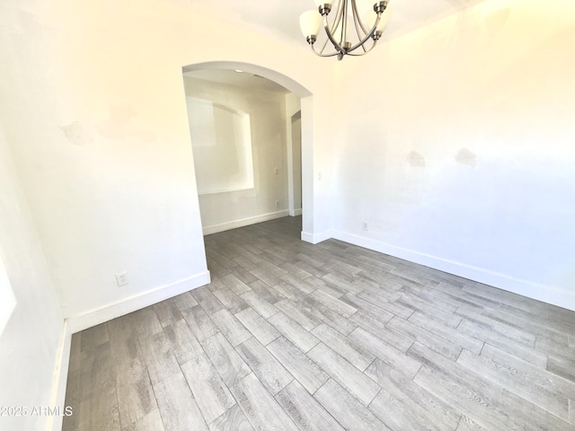 7116 W Sophie Ln, Laveen, AZ 85339 - unfurnished room featuring arched walkways, wood finished floors, a chandelier, and baseboards
