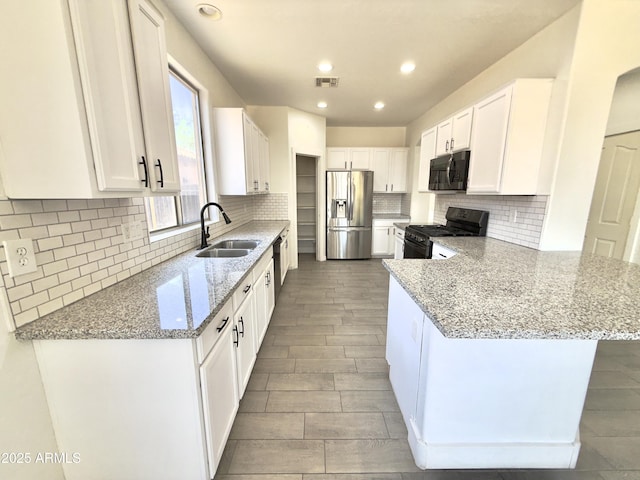 7116 W Sophie Ln, Laveen, AZ 85339 - kitchen with black appliances, a sink, a peninsula, light stone countertops, and white cabinets