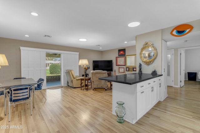 kitchen featuring light wood finished floors, dark countertops, visible vents, open floor plan, and white cabinetry