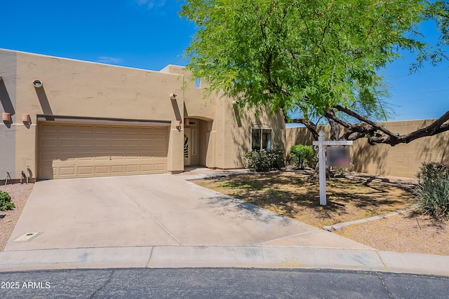 pueblo-style home featuring an attached garage, stucco siding, and concrete driveway