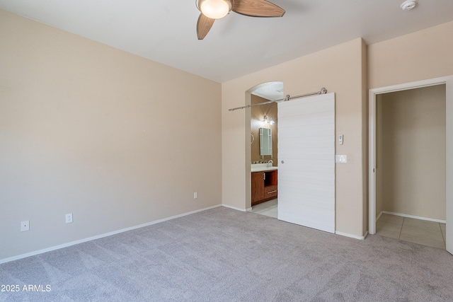 unfurnished bedroom with baseboards, ensuite bathroom, ceiling fan, and light colored carpet