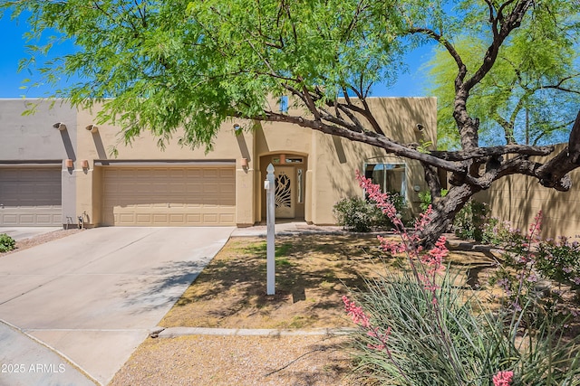 pueblo revival-style home featuring a garage, stucco siding, and driveway
