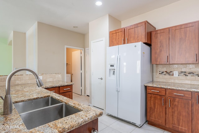 kitchen with light tile patterned flooring, light stone counters, a sink, white refrigerator with ice dispenser, and tasteful backsplash