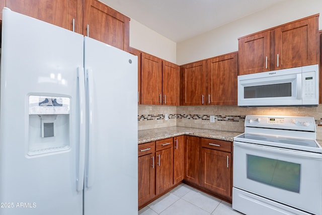 kitchen with brown cabinets, light stone countertops, white appliances, decorative backsplash, and light tile patterned floors