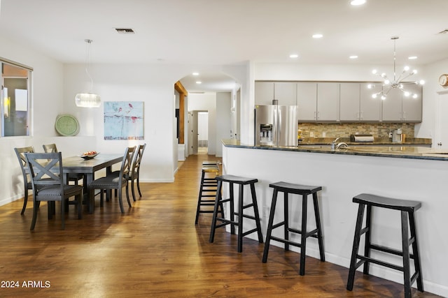 kitchen featuring a breakfast bar area, stainless steel refrigerator with ice dispenser, decorative backsplash, and decorative light fixtures