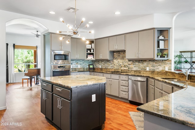 kitchen with dark stone counters, appliances with stainless steel finishes, a center island, open shelves, and a sink