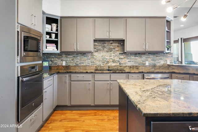 kitchen featuring appliances with stainless steel finishes, light wood-type flooring, backsplash, dark stone counters, and open shelves