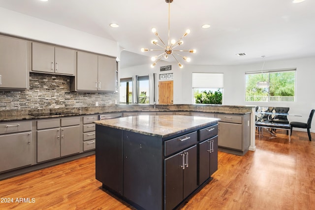 kitchen with hanging light fixtures, light stone countertops, a kitchen island, and black electric cooktop