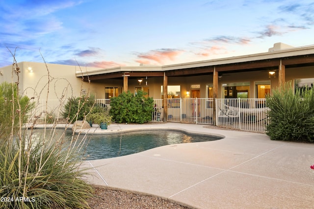 pool at dusk with a patio area, fence, and an outdoor pool