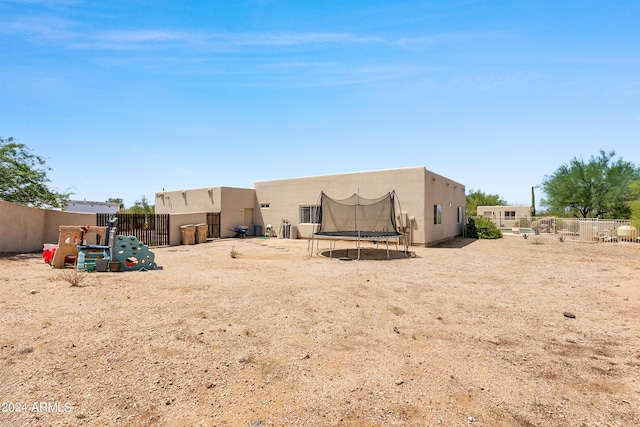 back of house featuring a trampoline, a playground, fence, and stucco siding