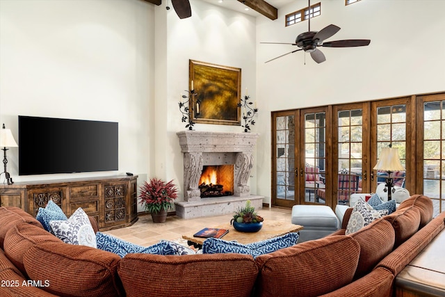 living room featuring beam ceiling, ceiling fan, a towering ceiling, and a fireplace