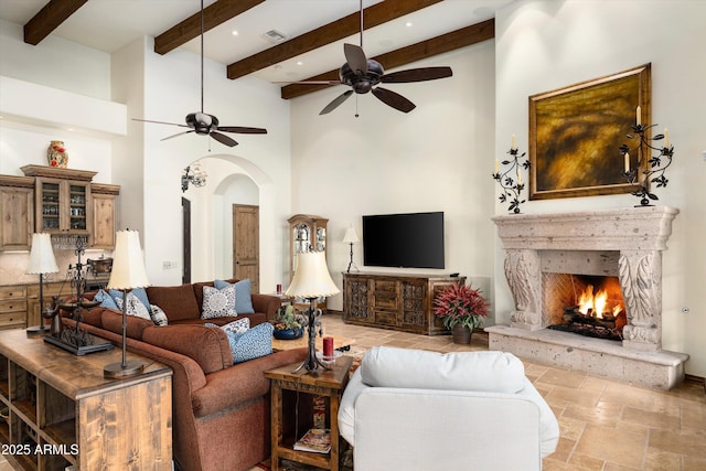 living room with a high ceiling, ceiling fan, a high end fireplace, and beamed ceiling